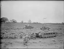 In the foreground, a group of soldiers crouch behind a tank. Another group, barely visible, crouch behind another tank in the background.
