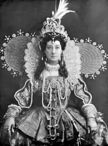 middle-aged white woman in extremely elborate 17th-century costume, staring balefully at the viewer