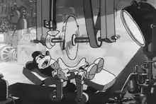 A black and white screenshot of Mickey Mouse retracting his stomach inward as a buzz-saw attempts to cut him in half.