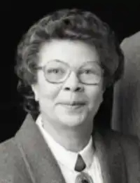 Head shot of Milon who has shirt curly hair and is wearing a dark jacket and a white shirt