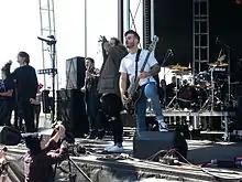 One man playing guitar, one man playing bass guitar, two men singing and one man playing drums on a stage