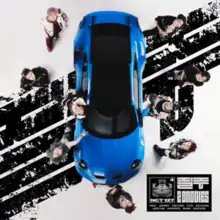 A photo from above of a blue sports car with the band members stood around it looking up at the camera