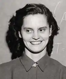 A young white woman with dark hair, smiling in front of a chalkboard.