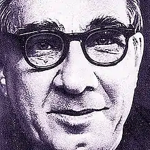 A middle-aged man in a jacket. He is looking down, slightly turned to his right