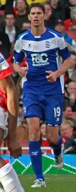 White man wearing blue and white sports clothing running.