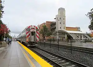 A train at a railroad station with a parking garage behind