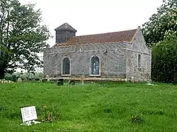 A small simple rectangular brick church seen from the southeast with two round-headed windows on the south side and a bellcote on the west gable