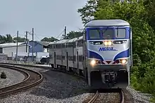 An outbound North Central Service train approaches the Schiller Park station in June 2019, being led by an Ex-Amtrak EMD F59PHI