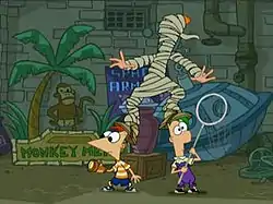 Two cartoon boys stand beside each other looking in opposite directions. A cartoon girl with orange hair stands clumsily on their heads, wrapped in raggy toilet paper. Behind them are pipes, a gray brick wall, and signs.