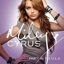 A teenage girl with long, curly brunette hair and a gray T-shirt faces the front as she touches her head with her left hand and waist with her right. Letters in the center of the image overlapping the girl's chest spell "Miley Cyrus" in cursive while "Party in the U.S.A." is spelled in print in the bottom right corner. The image has a lavender background.