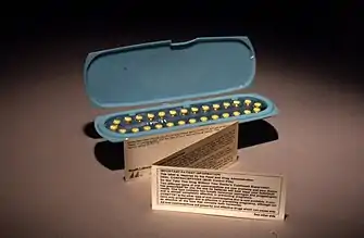 An oblong blue container holding 28 yellow pills, with a small, folded paper note standing in front of it