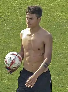 A man without shirts and holding ball on his hand with a green field on the background