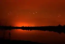 A red sky reflected in a lake at night, with short time-lapse trails of brighter stars