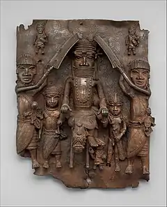 Plaque equestrian an Oba on horseback with attendants; between 1550 and 1680; brass; height: 49.5&nbsp;cm (19.mw-parser-output .frac{white-space:nowrap}.mw-parser-output .frac .num,.mw-parser-output .frac .den{font-size:80%;line-height:0;vertical-align:super}.mw-parser-output .frac .den{vertical-align:sub}.mw-parser-output .sr-only{border:0;clip:rect(0,0,0,0);clip-path:polygon(0px 0px,0px 0px,0px 0px);height:1px;margin:-1px;overflow:hidden;padding:0;position:absolute;width:1px}7⁄16 in.), width: 41.9 (16.mw-parser-output .frac{white-space:nowrap}.mw-parser-output .frac .num,.mw-parser-output .frac .den{font-size:80%;line-height:0;vertical-align:super}.mw-parser-output .frac .den{vertical-align:sub}.mw-parser-output .sr-only{border:0;clip:rect(0,0,0,0);clip-path:polygon(0px 0px,0px 0px,0px 0px);height:1px;margin:-1px;overflow:hidden;padding:0;position:absolute;width:1px}1⁄2 in.), diameter: 11.4&nbsp;cm (4.mw-parser-output .frac{white-space:nowrap}.mw-parser-output .frac .num,.mw-parser-output .frac .den{font-size:80%;line-height:0;vertical-align:super}.mw-parser-output .frac .den{vertical-align:sub}.mw-parser-output .sr-only{border:0;clip:rect(0,0,0,0);clip-path:polygon(0px 0px,0px 0px,0px 0px);height:1px;margin:-1px;overflow:hidden;padding:0;position:absolute;width:1px}1⁄2 in.); Metropolitan Museum of Art