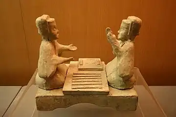 Han dynasty glazed pottery tomb figurines playing liubo, with six sticks laid out to the side of the game board