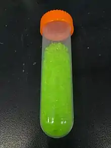yellowish green crystals in a transparent vial with an orange ribbed screw on cap