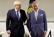 Charles standing next to Boris Johnson with the flag of the Commonwealth of Nations behind them
