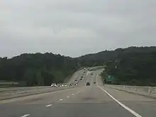 Downhill view of a four-lane divided freeway; the opposing lanes of traffic are separated by concrete barriers.