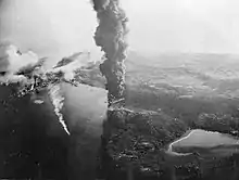 Black and white aerial photograph of smoke rising from a port town