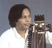 Narayan looks to the side with a sarangi held close to his body.