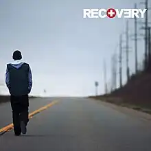 The cover features Eminem walking down the road under clear blue sky. On top-left corner, in bold and capitalised format, the title RECOVERY appears.