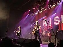 Rise Against performing on stage. Three band members can be seen, while the fourth is partially obscured.