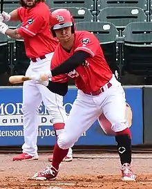 A baseball player in a red baseball uniform and baseball helmet and white pants swinging at a pitch