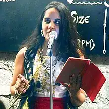 Rochelle Potkar standing at a microphone, holding a book