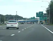 Ground-level view of four lanes of a busy freeway; several green exit signs and two overpass bridges are visible in the distance.