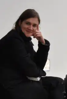 A woman with dark hair smiling, sitting next to a film camera