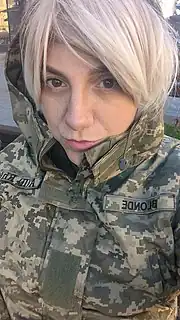 Ashton-Cirillo, in a black top and white cardigan, with her hair red, purses her lips.