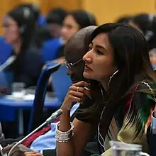 Woman sitting among a group of people at a table with a mic in front of her