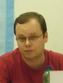 short-haired white male wearing glasses and red t-shirt, looking at camera