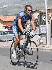 A cyclist riding while holding his helmet.
