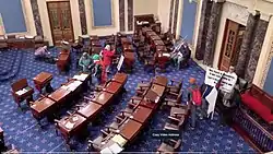 4 rioters stand in an empty Senate chamber.