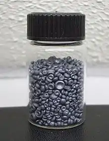 A small glass jar filled with small dull grey concave buttons. The pieces of selenium look like tiny mushrooms without their stems.