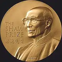 A gold circular medal with a depiction of an elderly man with glasses wearing a jacket buttoned to the neck; the English words "The Shaw Prize" and Chinese characters "邵逸夫獎" engraved on it