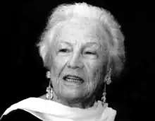 Black and white portrait of Silvana Lattmann. Head and shoulders of distinguished older woman with scarf draped elegantly over neck. She has short light-coloured hair and is wearing dangling earrings.