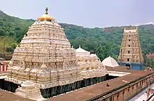 A three-tier yellow coloured pyramid like structure with sculptures and carvings to the left and a five tier tower to the right.