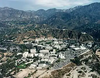 An image featuring a birds-eye, aerial view of the laboratory campus buildings and surrounding landscape. The site is nestled in a valley between green, rolling mountains.