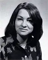 A formal pose of a young woman in her early twenties, dark straight hair parted near the center, wearing a dark floral print top.