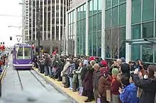 A large crowd of people on a station platform waiting for an approaching streetcar.