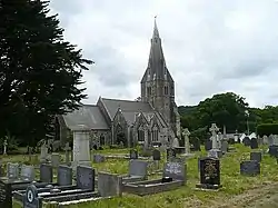 A medium-sized church with a tall stone steeple in a graveyard.
