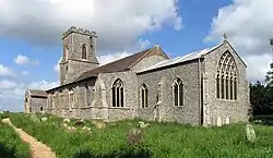 A stone church seen from the southeast, showing the chancel, beyond which is a taller nave with a south aisle and porch, and a battlemented tower