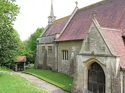 Part of a church built in stone with red tiles and a short spire