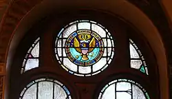 A half dark blue, half light blue circle with the words Collegium Georgiopolitanum 1789 inscribed around the edge in gold with a gold federal eagle in the center holding a cross and a globe in its talons, and a scroll with the motto Utraque Unum in its beak. Sixteen gold stars are arranged around the eagle, and a gold instrument above it.