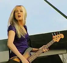 A 32-year-old woman is playing a four-string electric bass guitar.