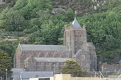 A large church standing before a hillside, with a clerestory and, to the left a tower with a pyramidal roof.