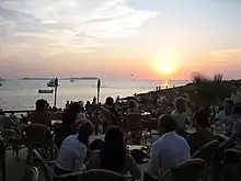 People sitting at tables. The sun approaches the horizon.