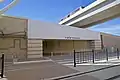 Pedestrian crosswalk and entrance to airport Terminal B. Just north of the platform, the DFW Skylink elevated track passes over the TEXRail tracks.